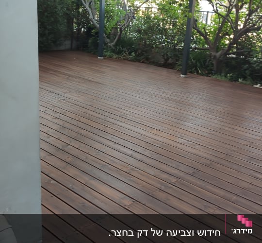 רצפת עץ עם פרגולה וגינה ברקע